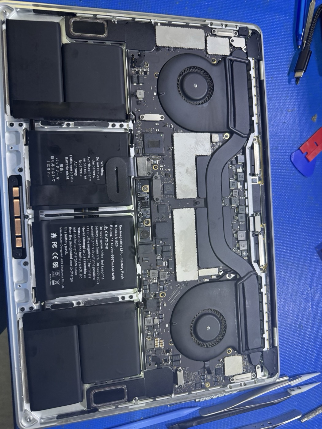Open MacBook repair with internal fans, battery, and logic board visible